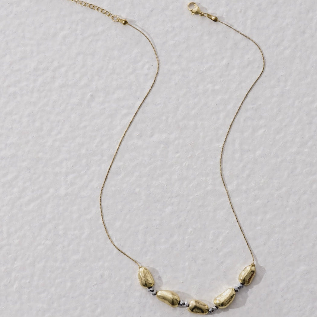 Necklace with gold chain and stone beads on a textured gray background