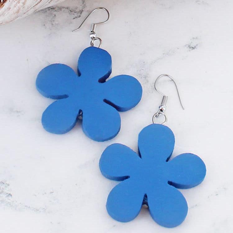 Blue flower-shaped earrings on a marble surface with bread in the background