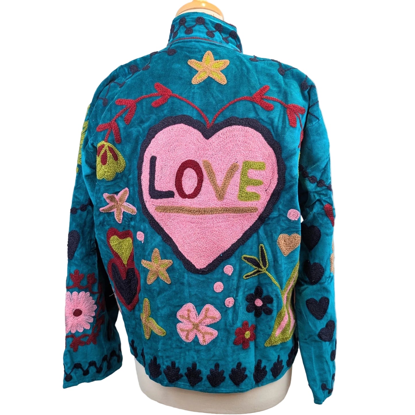 A teal quilted jacket displayed on a mannequin, featuring a large pink heart on the back with the word 'LOVE' embroidered inside, surrounded by colorful floral and heart motifs.