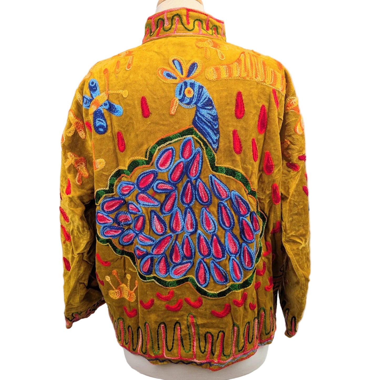 A mustard yellow velvet jacket with a colorful embroidered peacock design on the back, displayed on a mannequin against a plain white background.