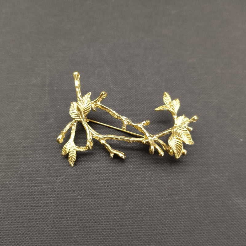 Gold leaf branch brooch on a dark gray background